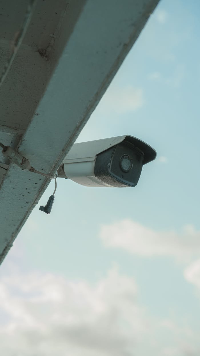our-story A security camera mounted on a building eaves under a clear blue sky.